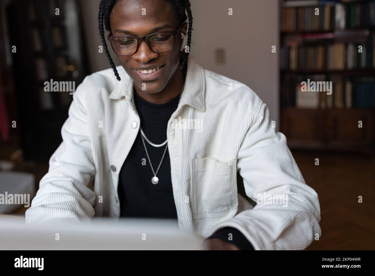 Sorridente giovane uomo africano felice in occhiali utilizzando il portatile a casa, trascorrere il tempo libero su Internet Foto Stock