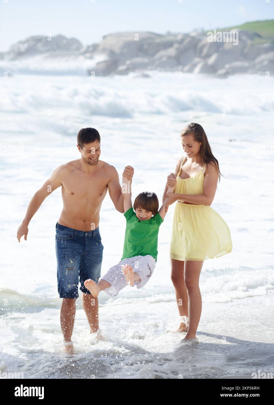 Wheee. Due genitori che oscillano il loro figlio tra loro mentre camminano lungo la spiaggia. Foto Stock