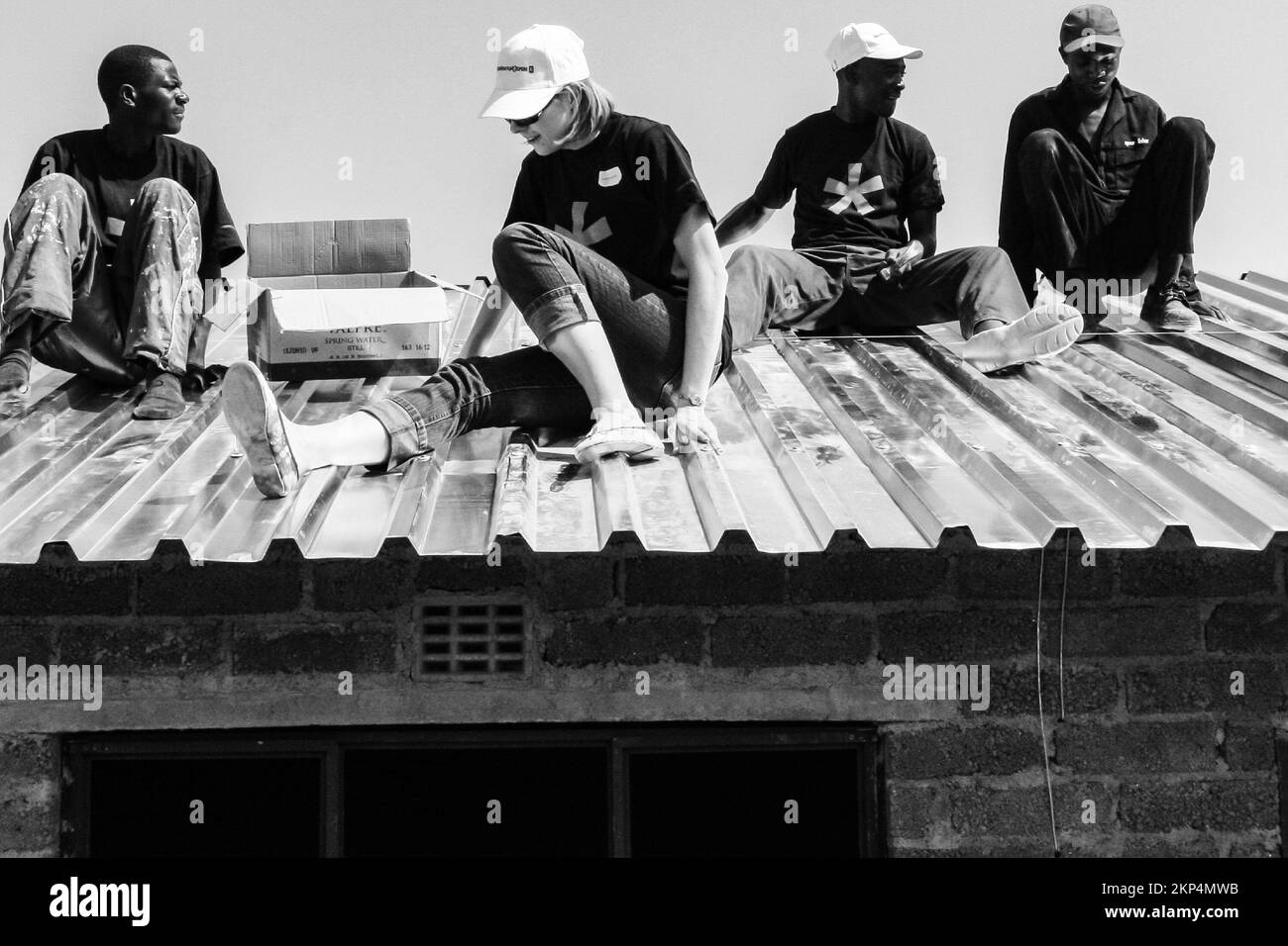 Una visione di diverse comunità di sensibilizzazione programma persone che aiutano a installare tetto in metallo su una piccola casa Foto Stock