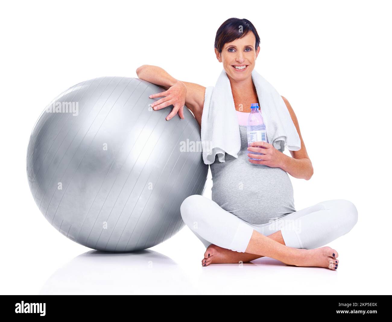 Mantenendosi in forma, fino al suo trimestre finale. Una madre incinta sorridendo con una palla pilates mentre isolato su bianco. Foto Stock
