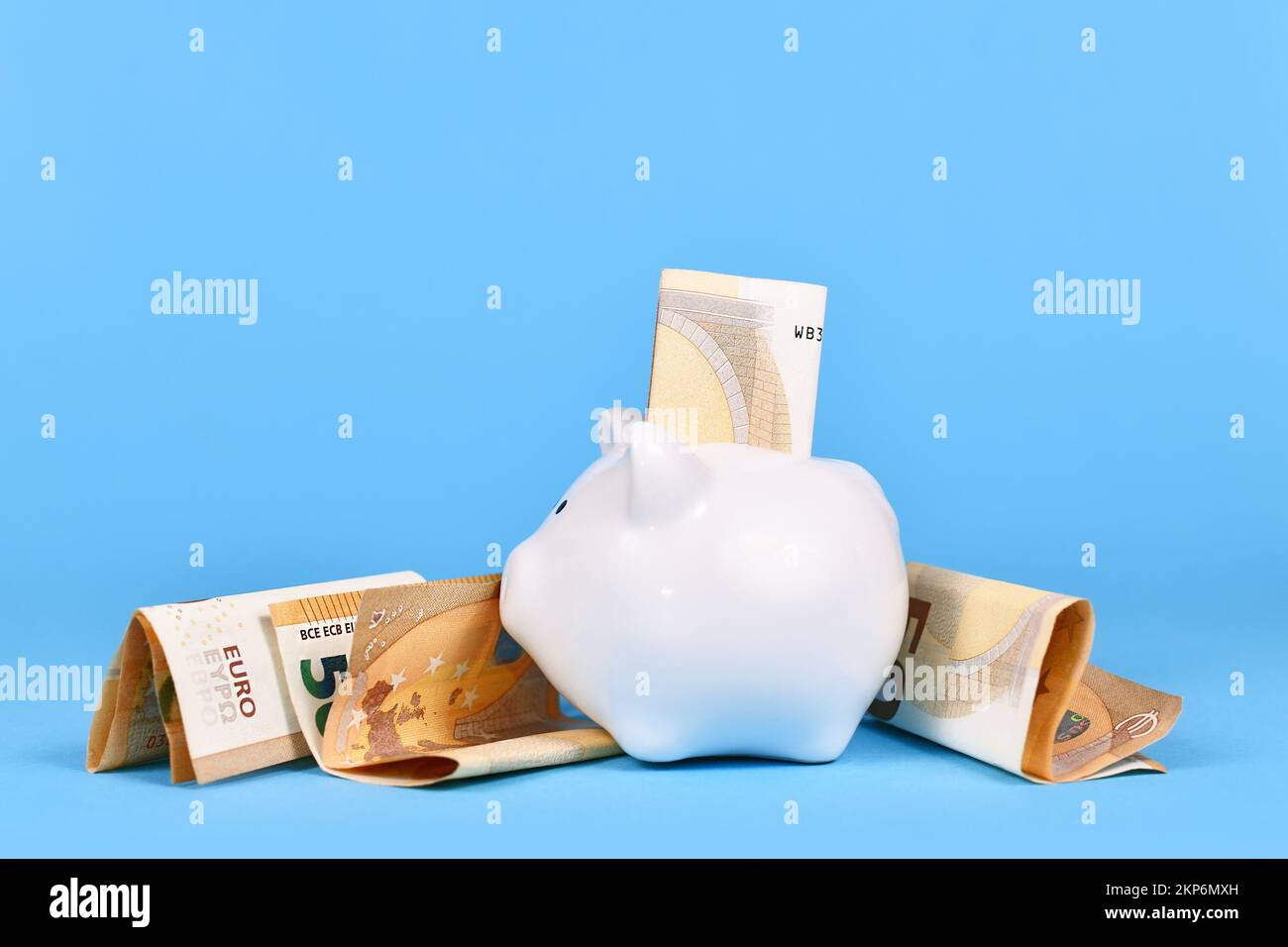 Concetto di risparmio economico. Banca di piggy bianco con fatture da 50 euro su sfondo blu Foto Stock