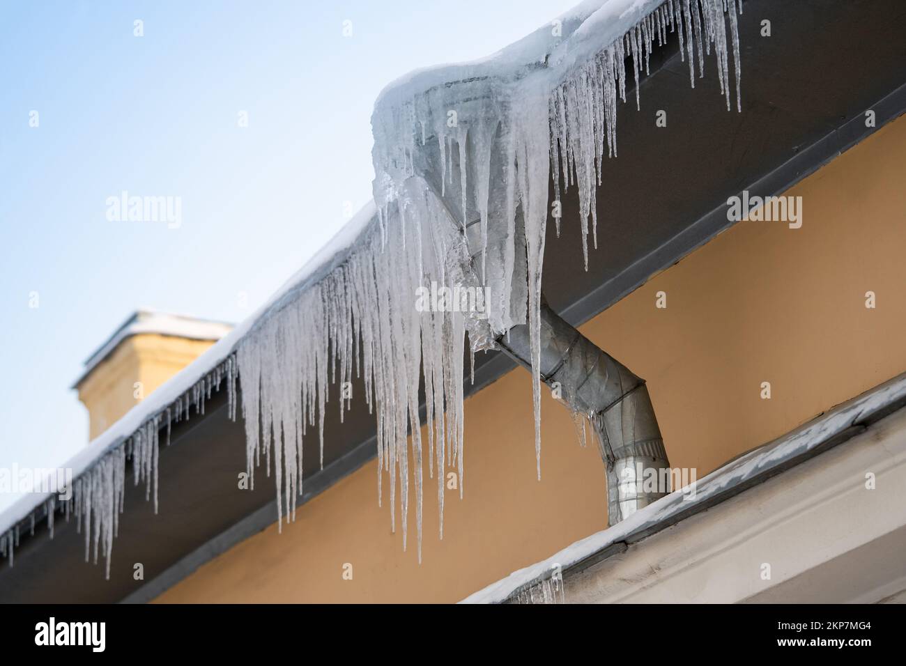 Grandi ghiacciate che pendono pericolosamente dal bordo della costruzione nella fredda giornata invernale. Diga di ghiaccio sul tetto Foto Stock