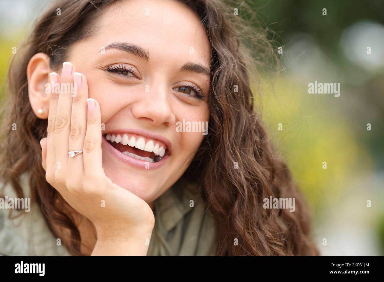 Donna felice sorridente alla macchina fotografica che mostra l'anello di fidanzamento in un parco Foto Stock