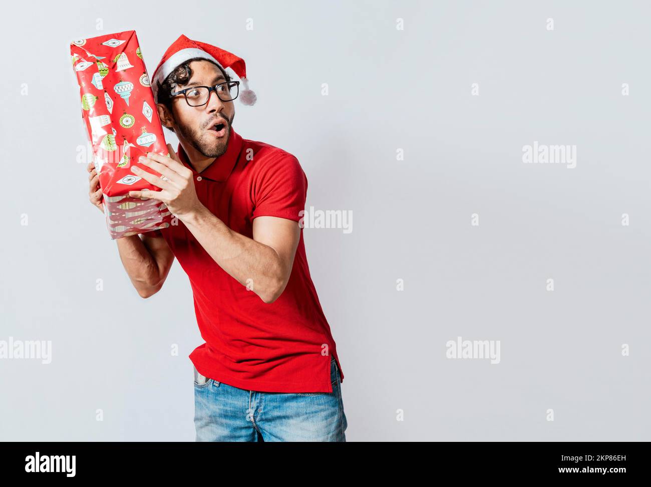 Uomo di Natale che tiene e ascolta una confezione regalo. Ragazzo di Natale che tiene e ascolta una confezione regalo. Entusiasta gente di natale che tiene e ascolta un regalo. Foto Stock