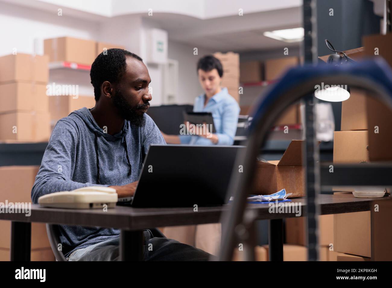 Dipendente che controlla lo stato del prodotto prima della consegna al cliente, controllando i dettagli di spedizione sul computer portatile. Responsabile del reparto di consegna che lavora in magazzino Foto Stock