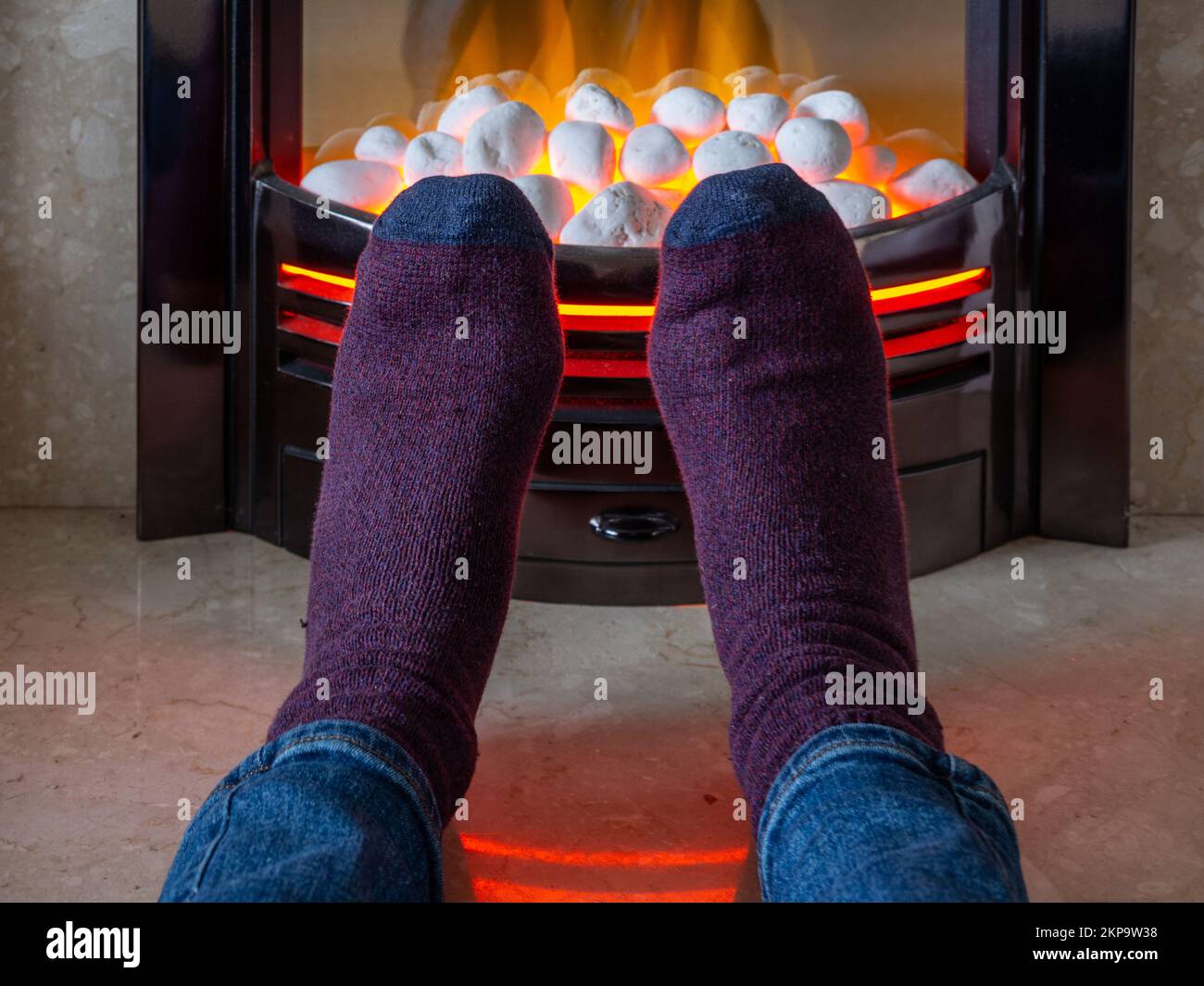 Uomo che scalda i piedi di fronte a un incendio a effetto carbone elettrico per evitare di accendere il riscaldamento centrale; crisi energetica del Regno Unito 2022. Foto Stock