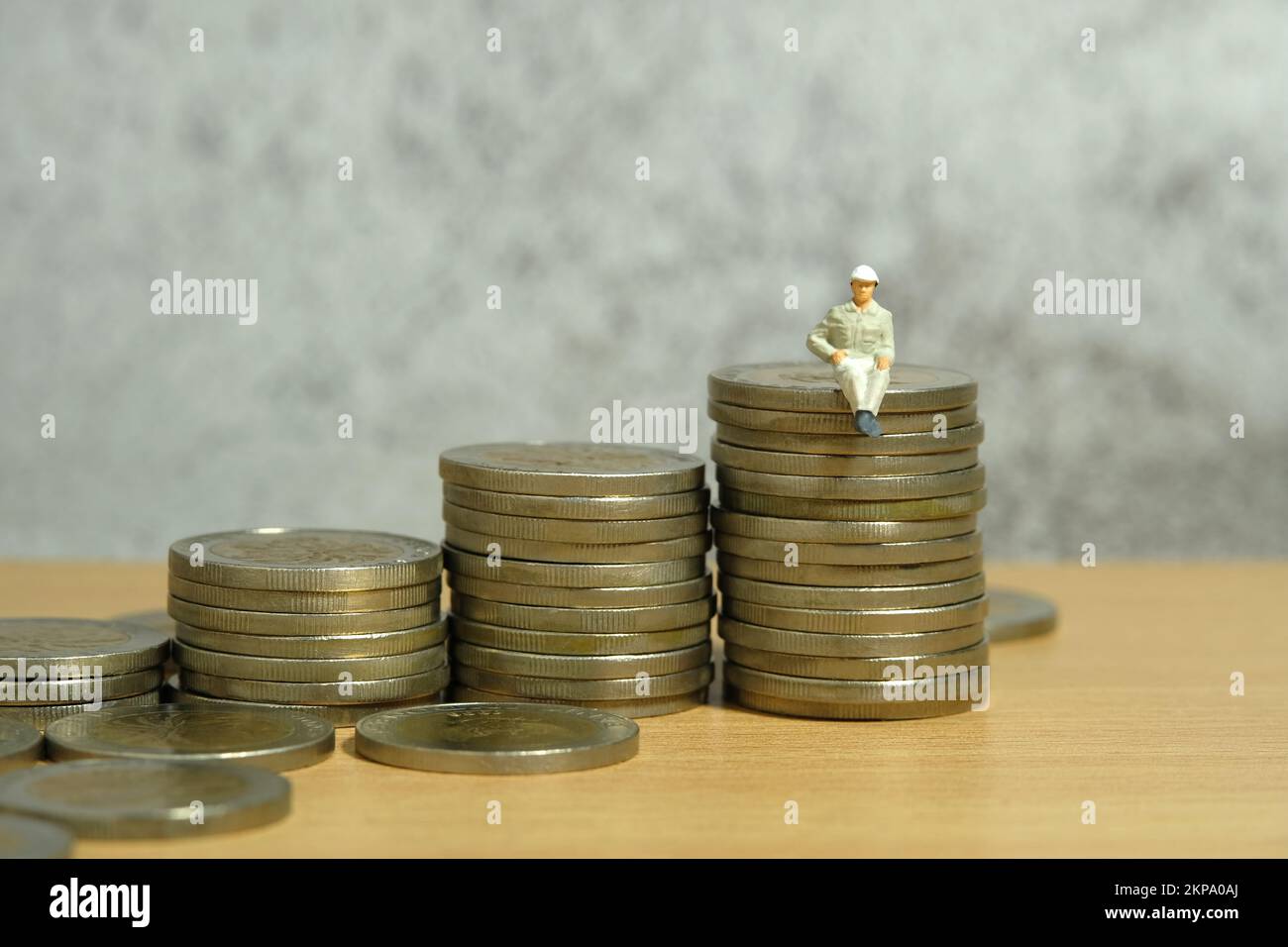 Fotografia di figura giocattolo delle persone in miniatura. Crescita del reddito e dello stipendio. Un lavoratore di uomini seduto sopra il mucchio di monete della scala. Foto dell'immagine Foto Stock