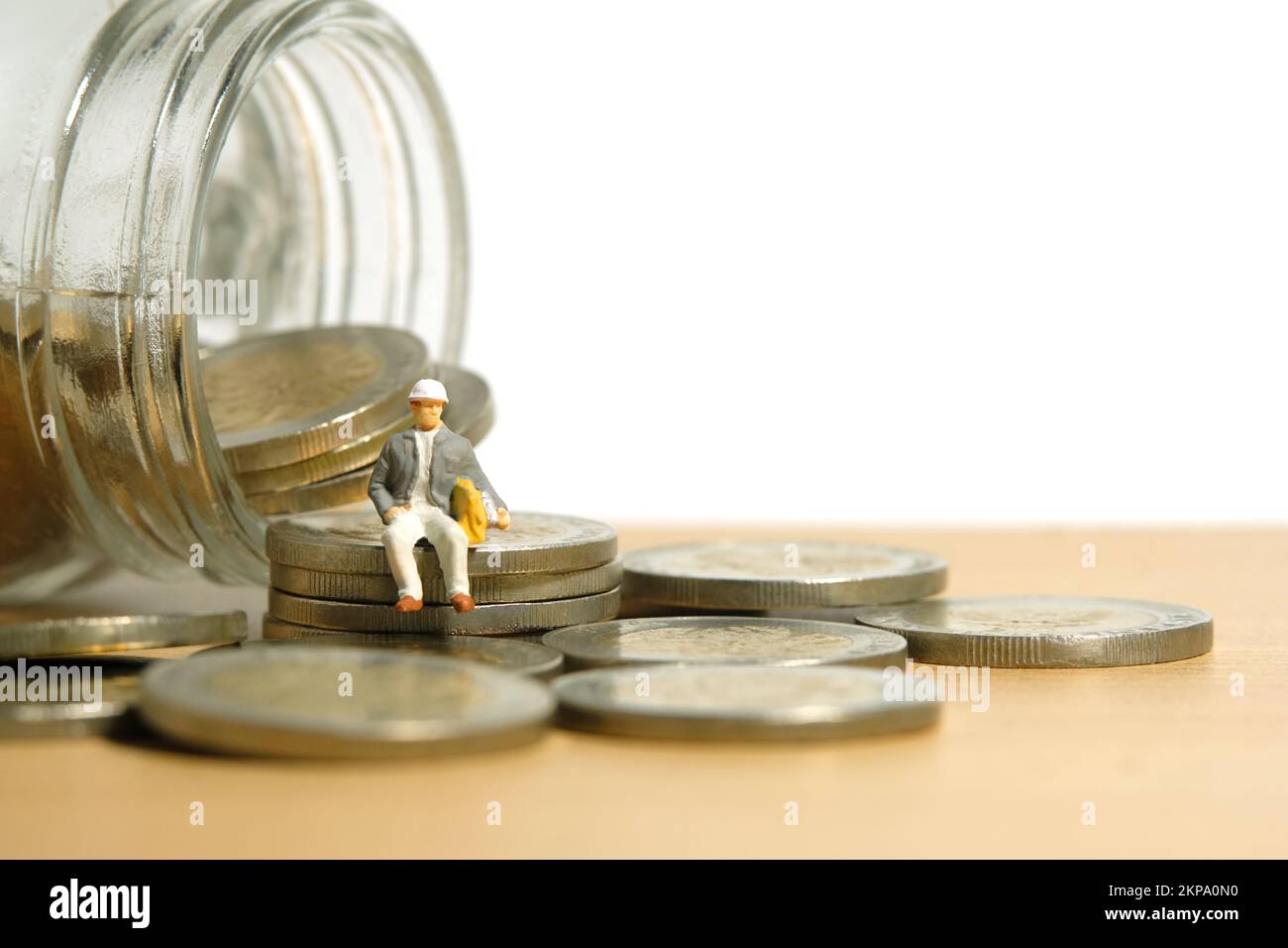 Fotografia di figura giocattolo delle persone in miniatura. Concetto di pensione e pensione. Gli uomini lavorano seduti sopra il mucchio di monete e il vaso di vetro su un tavolo da scrivania. Immagine Foto Stock