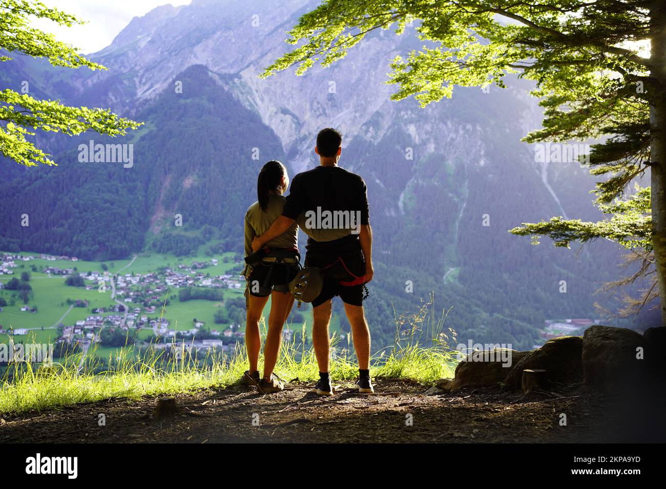 Vista sul retro di una coppia sportiva con un'attrezzatura da arrampicata via ferrata che guarda le montagne alla luce della sera Foto Stock