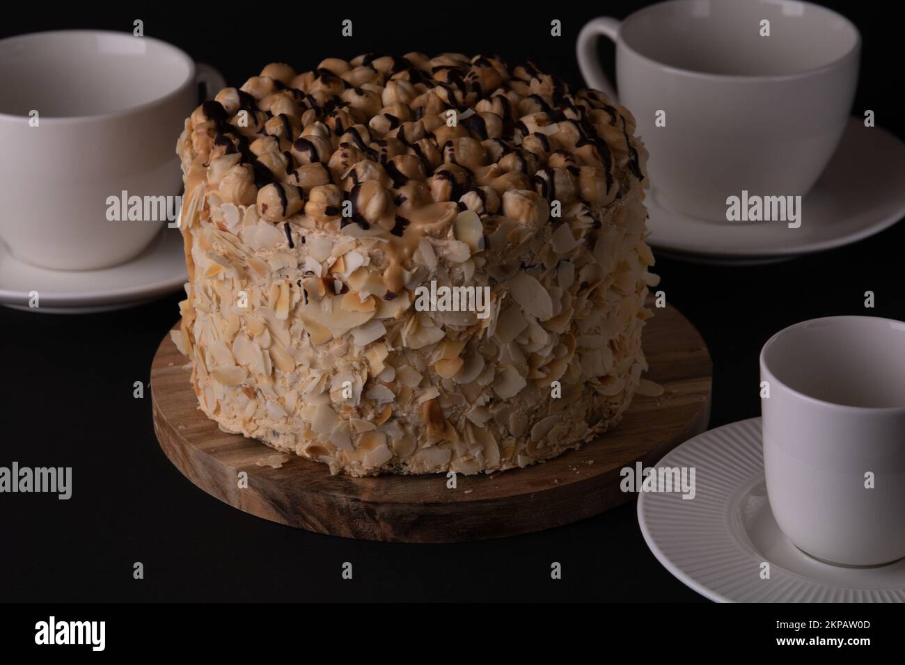 foto torta di noce rotonda con piatti tazze piattini cucchiai su sfondo nero Foto Stock