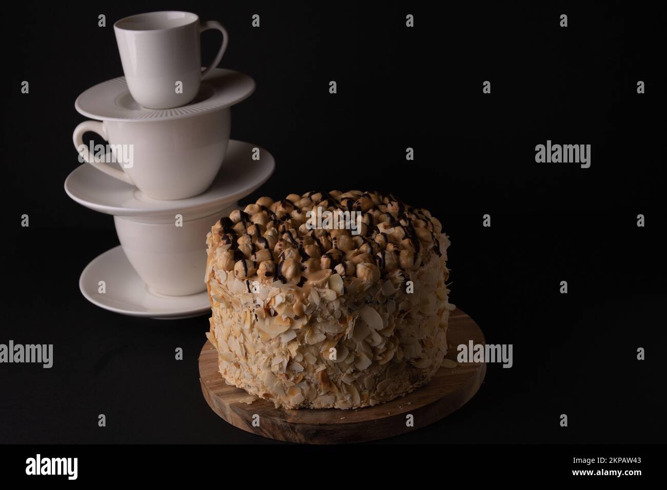 foto torta rotonda con piatti cucchiai piattini impilati in una fila verticale su uno sfondo nero Foto Stock