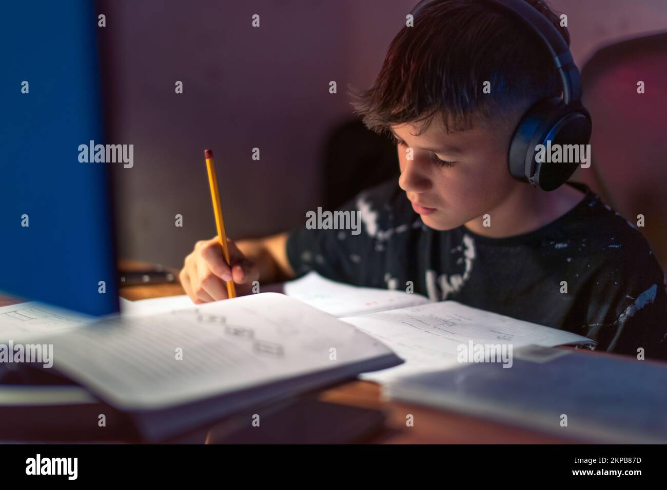 Ragazzo che fa i compiti mentre ascolta la musica con le cuffie Foto Stock