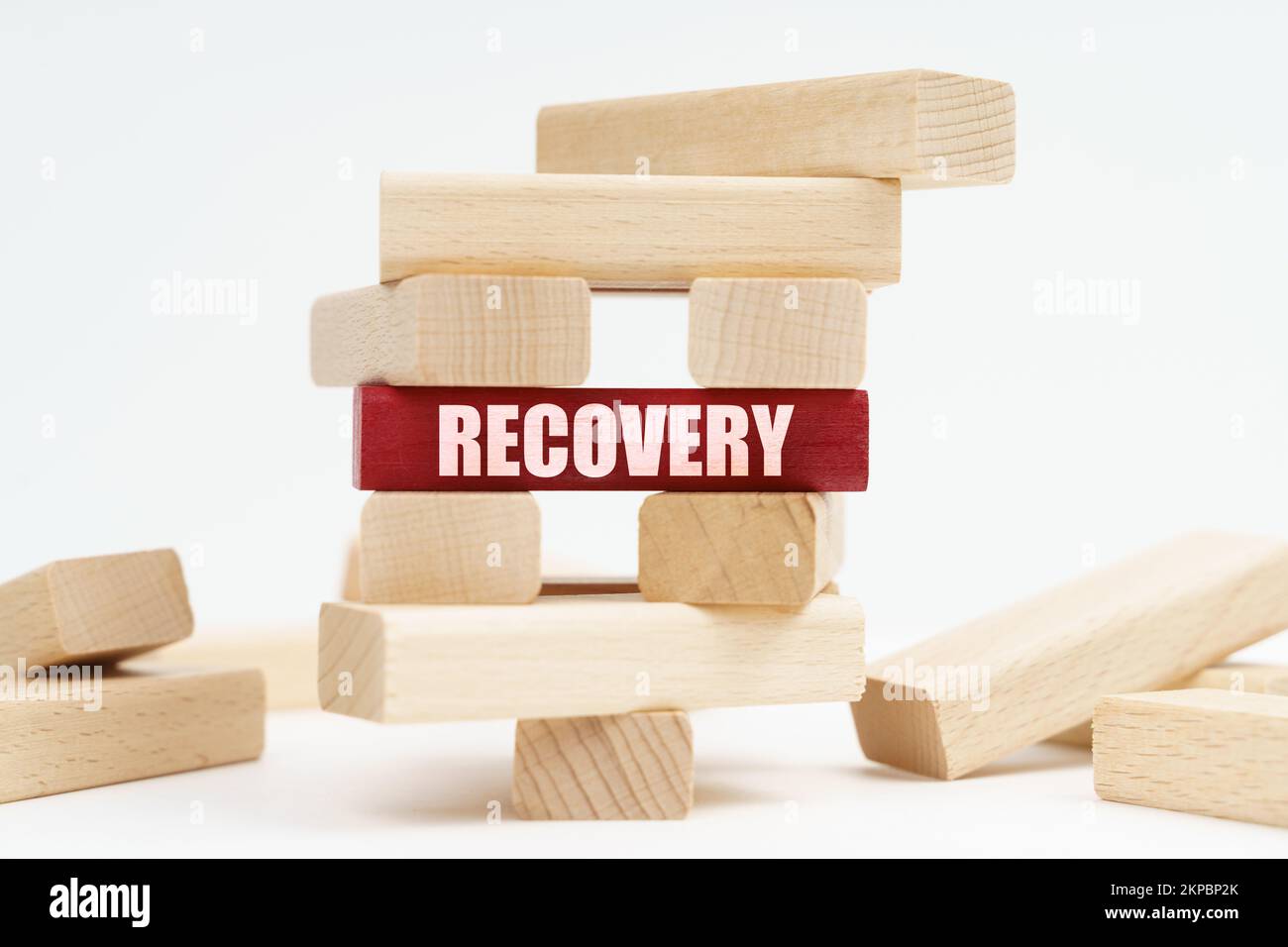 Concetto di business e finanza. Sulla superficie bianca si trova una torre di legno distrutta fatta di tavole, sulla lastra rossa si trova un'iscrizione - RECOVE Foto Stock
