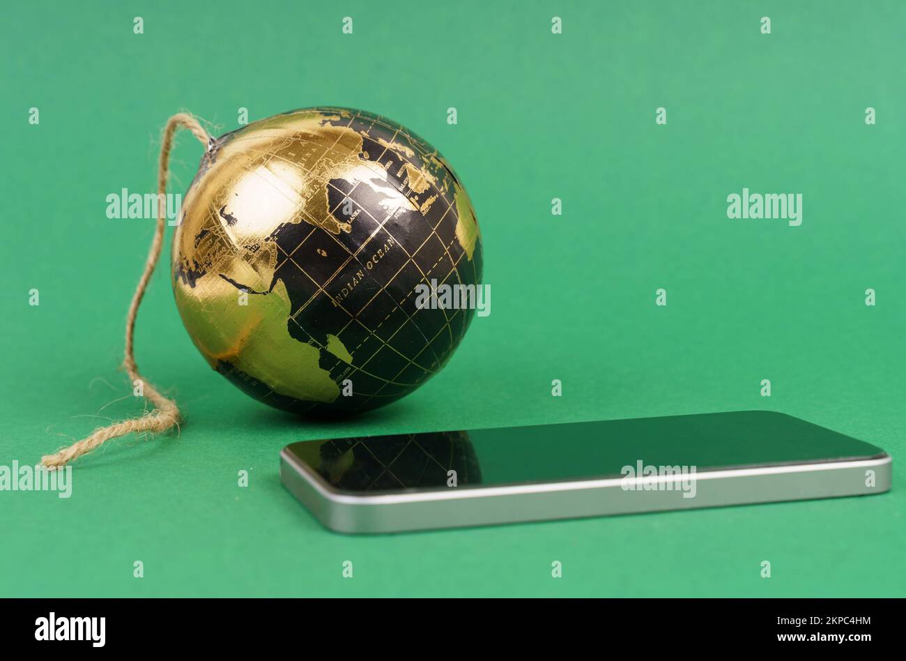 Concetto di innovazione futuristica globale. Sul tavolo c'è uno smartphone e un pianeta sotto forma di bomba con uno stoppino. Isolato su un backgroun verde Foto Stock