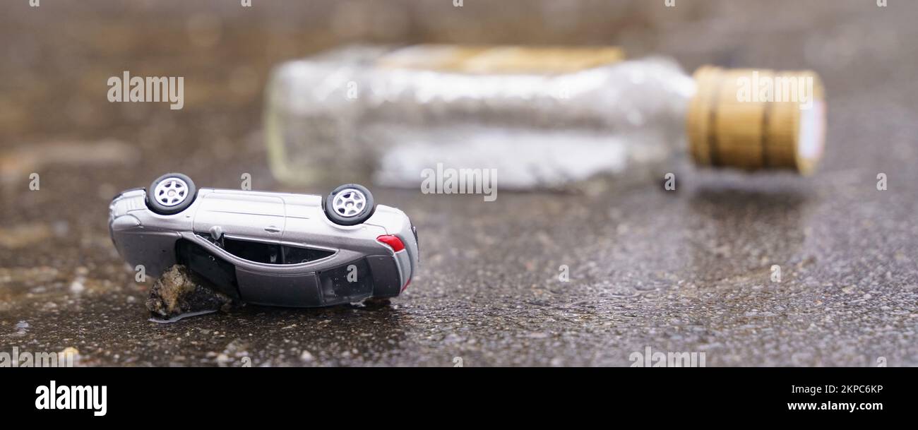 Occorrenza. Incidente stradale - un'auto ribaltata con una bottiglia di alcool sullo sfondo. Foto Stock