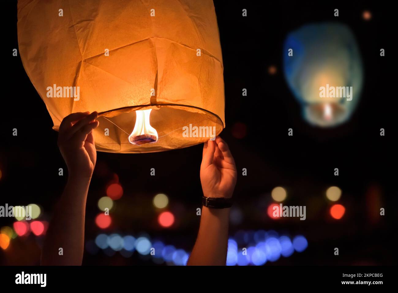 Le mani del giovane uomo rilasciano le lanterne del cielo sul festival. Luce calda dal fuoco Foto Stock