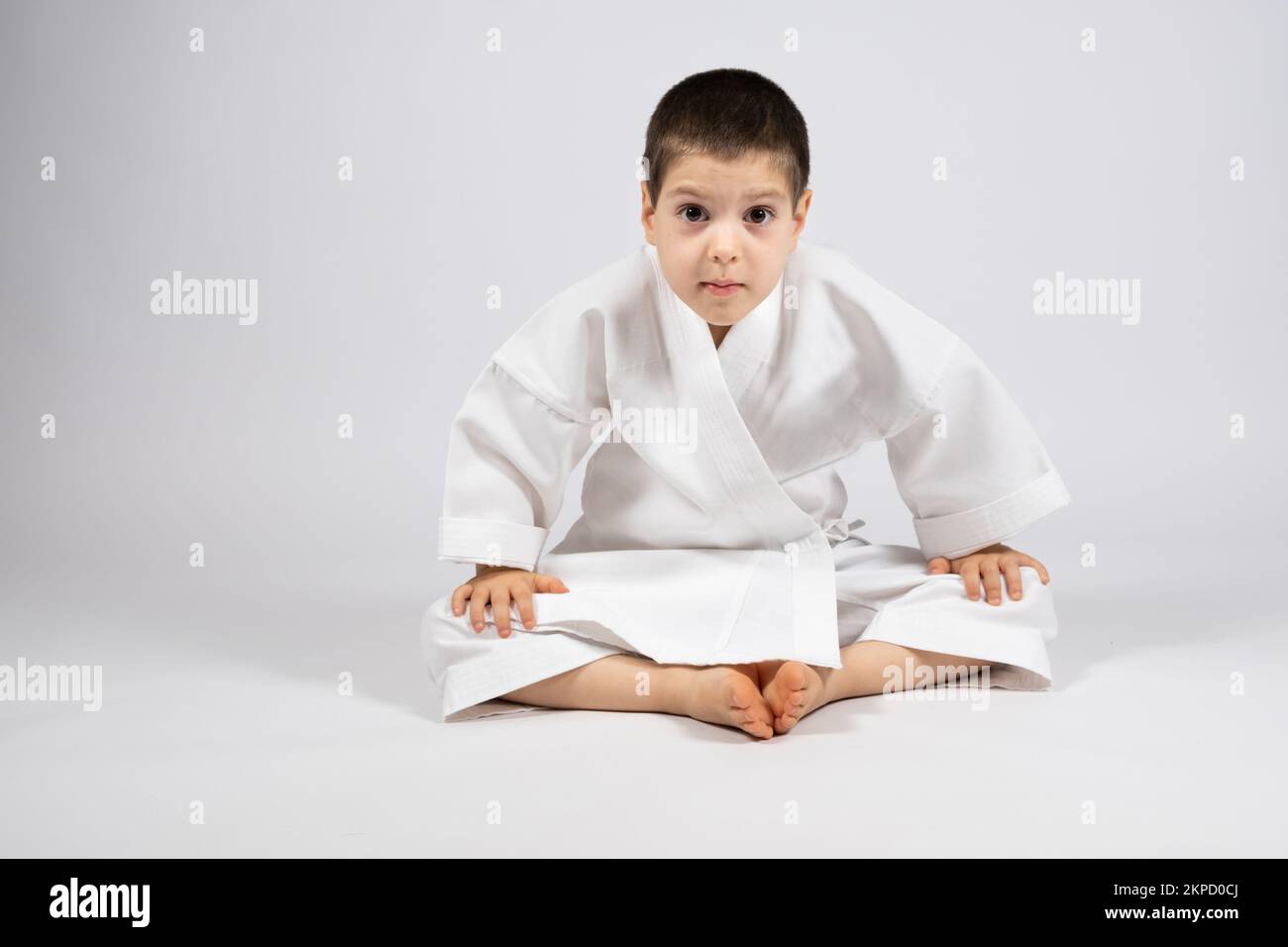 Un ragazzino in un kimono pratica il karate, siede in una posa a farfalla e pratica lo stretching, un posto per il testo. Foto Stock
