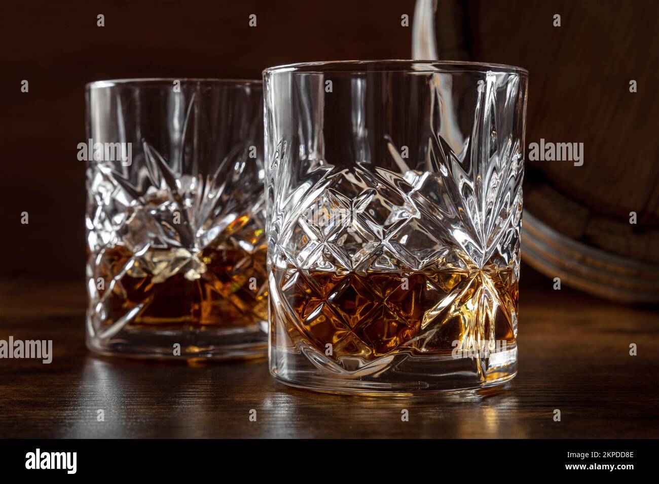 Sbattere nei bicchieri con un barile. Whisky borbonico e una botte su un fondo di legno rustico scuro, una degustazione in una distilleria Foto Stock