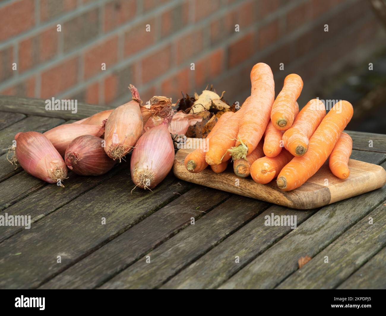 carote e scalogni fuori su un tavolo di legno Foto Stock