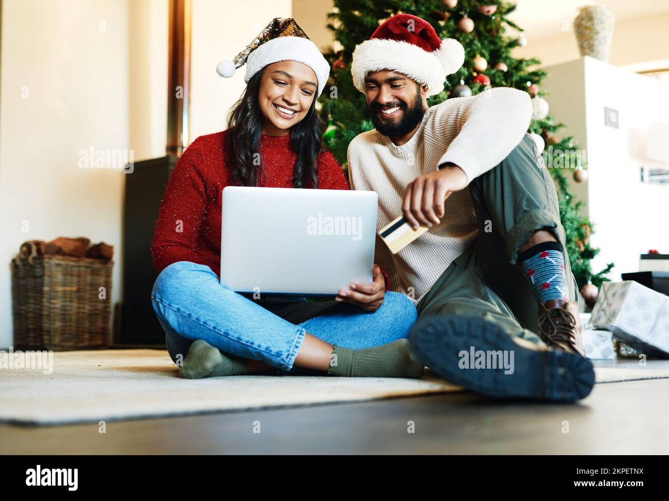 Laptop, carta di credito e coppia shopping online per regali di natale insieme seduti sul pavimento a casa. E-commerce, affari e giovani Foto Stock