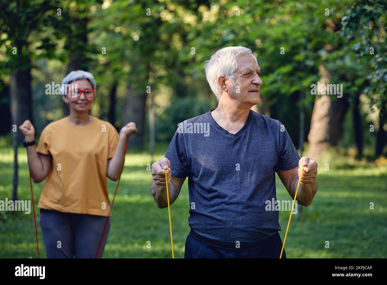 I coniugi senior 60 indossano abbigliamento sportivo che fa esercizi, armi da training all'aperto nel parco estivo al mattino utilizzando fasce di gomma resistente. Stile di vita sano Foto Stock