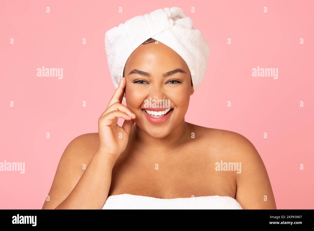 Bella afroamericana donna oversize con asciugamano bianco sulla testa, godendo la sua giovane bellezza e sorridendo alla macchina fotografica Foto Stock