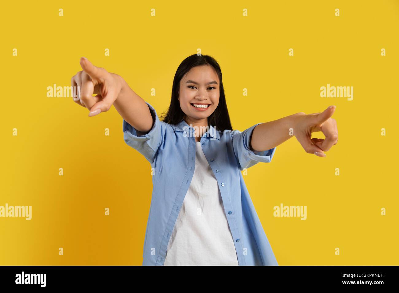 Felice fidato studente cinese donna millenario in casual punta dita alla macchina fotografica, ha divertimento Foto Stock
