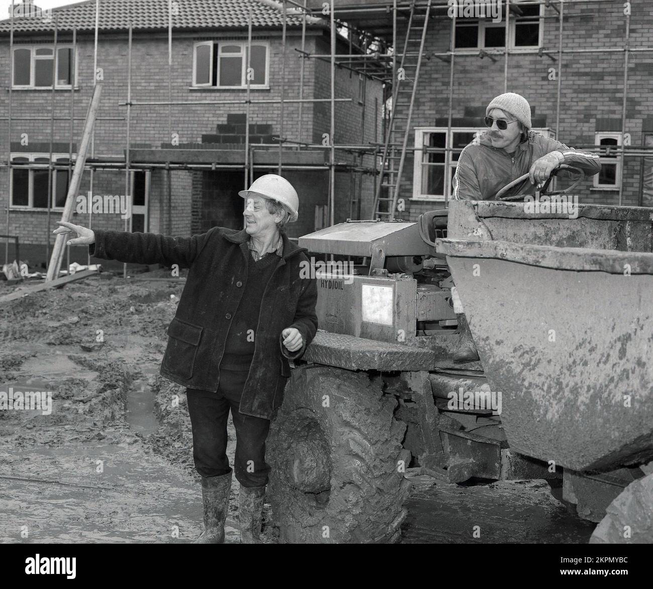 1980s, due costruttori in cantiere, in chat, uno seduto su un carrello di carico pesante, Inghilterra, Regno Unito. vuoi spostare un salto?? Foto Stock