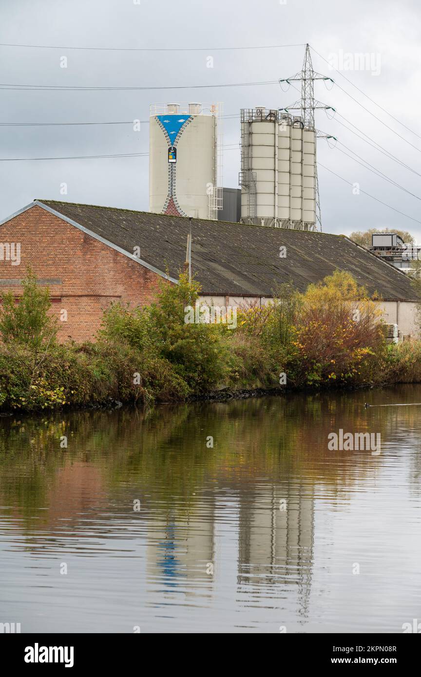 Gijzegem, Regione fiamminga orientale, 11 04 2022 - silo industriale e stoccaggio di massa che si riflette nelle acque del fiume Dender Foto Stock