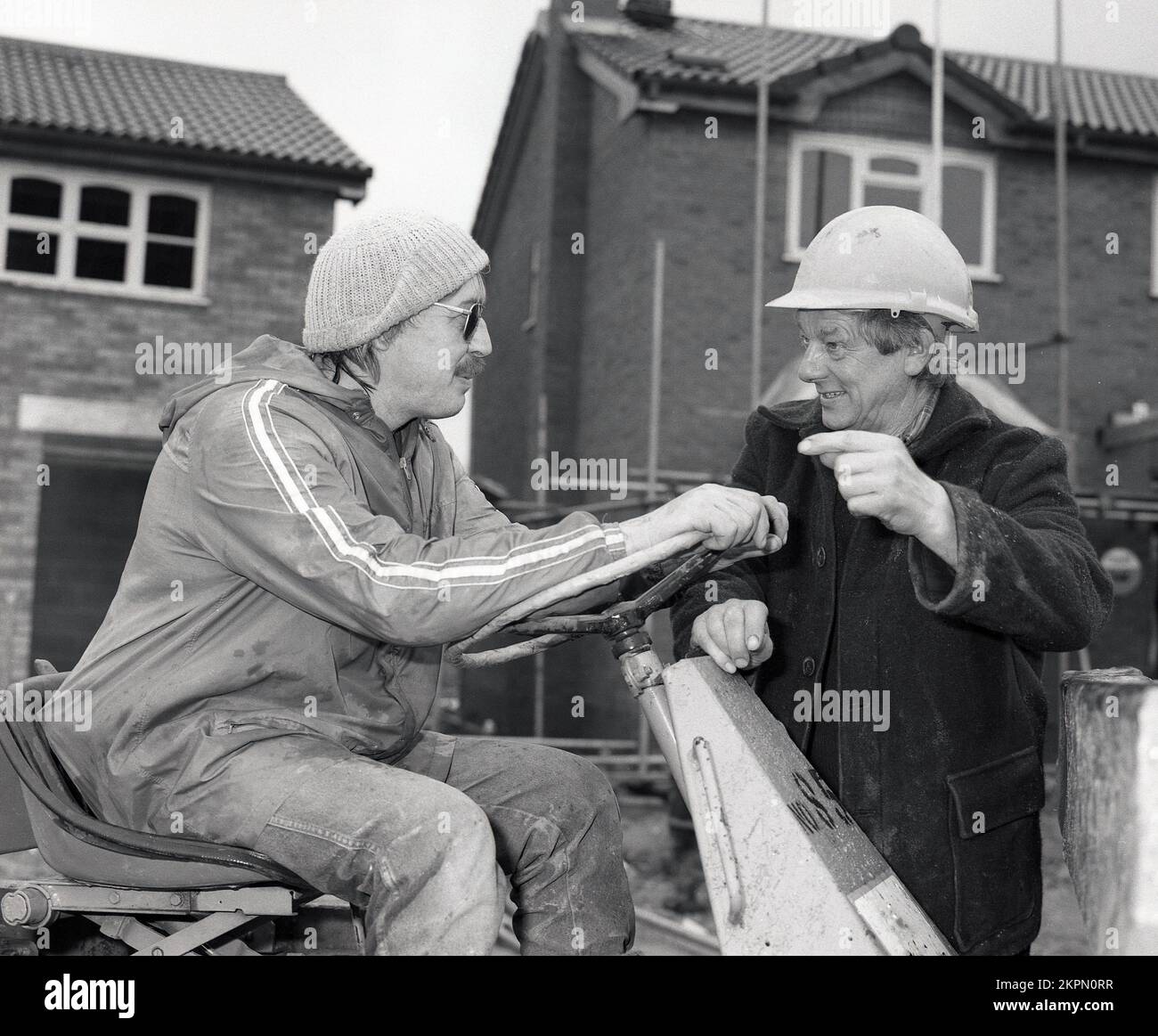 1980s, due costruttori sul sito di costruzione, chattando, avendo una risata, uno seduto su un carrello di carico?/pesante, Inghilterra, Regno Unito. vuoi spostare un salto?? Foto Stock