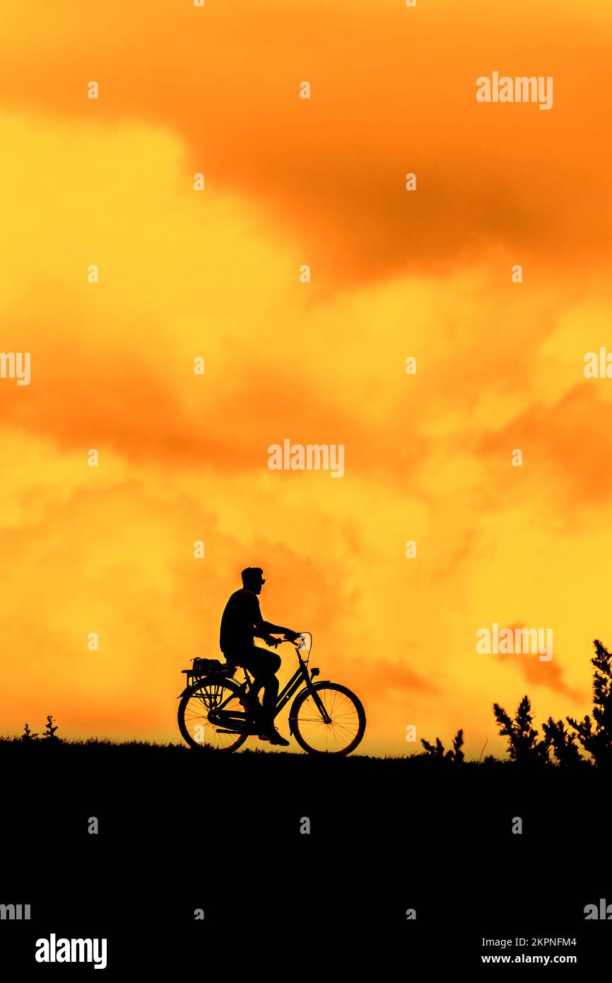 Ciclista maschile in bicicletta con la sua silhouette contro il cielo arancione del tramonto in estate Foto Stock
