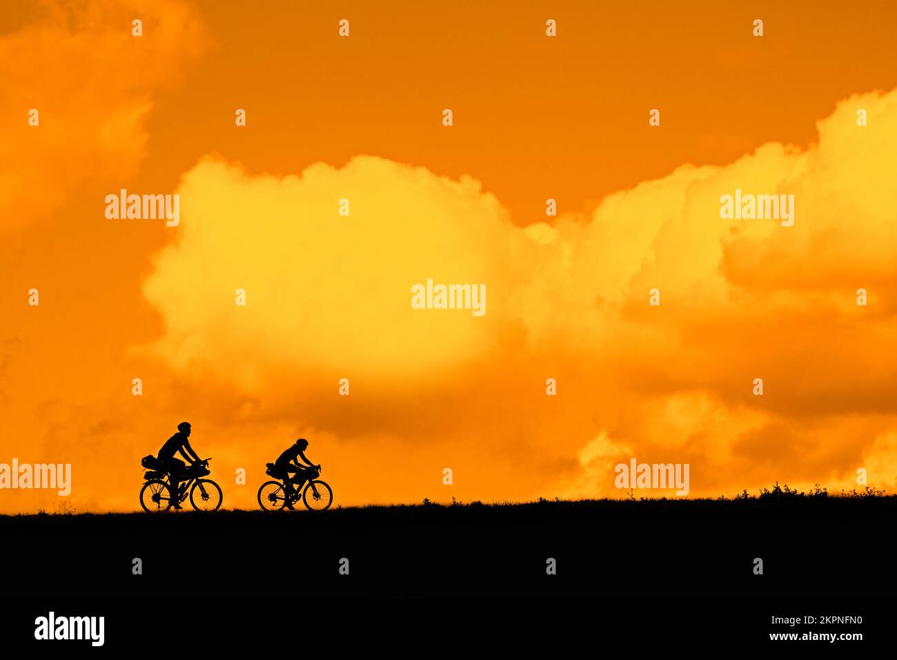 Un paio di giovani ciclisti in sella alle loro biciclette da turismo, in estate, si sono contestate contro il cielo arancione del tramonto Foto Stock