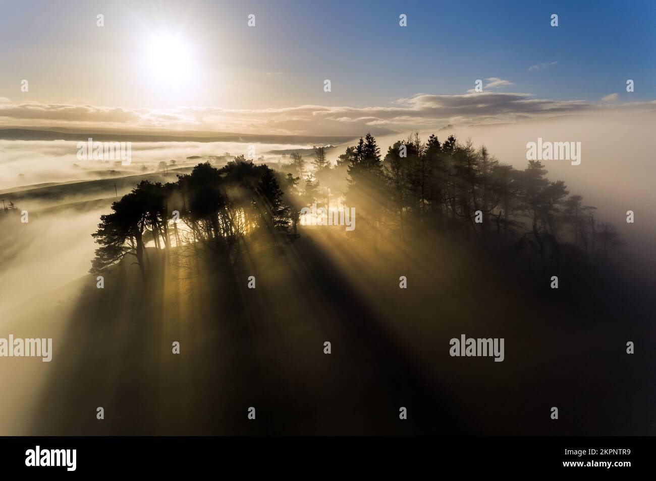 Kirkcarion, Lunedale, Teesdale, County Durham, Regno Unito. 28th novembre 2022. Meteo nel Regno Unito. Spettacolari raggi di luce illuminano l'antico tumulo coperto di alberi di Kirkcarion poco prima del tramonto. Credit: David Forster/Alamy Live News Foto Stock