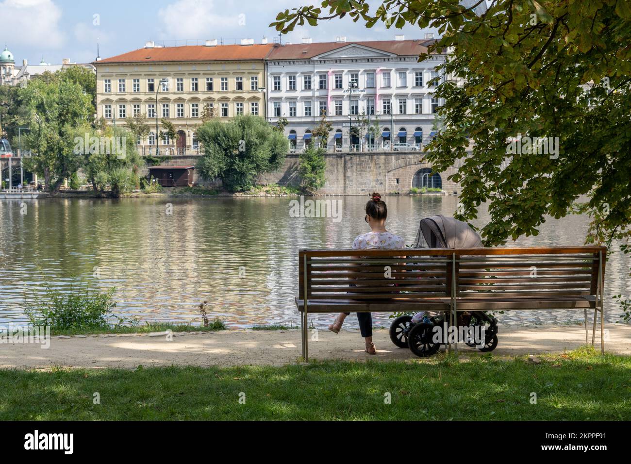 Praga, Repubblica Ceca - 5 settembre 2022: Madre con bambino seduta su panchina sul fiume Moldava Foto Stock