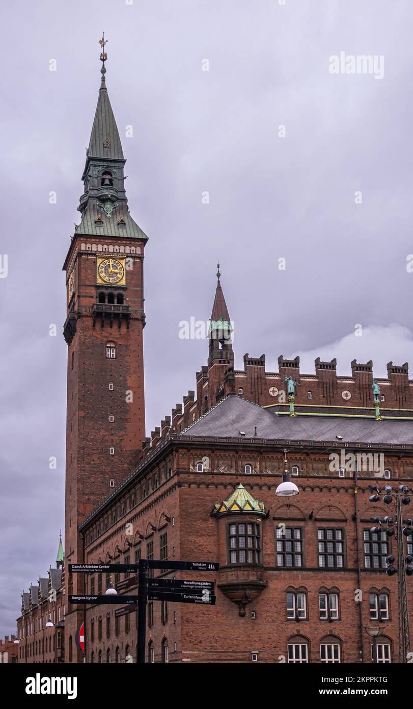 Copenaghen, Danimarca - 23 luglio 2022: Angolo nord-ovest del municipio di mattoni rossi con il suo alto campanile, con orologio dorato e guglia verde affilata, contro il grigio Foto Stock