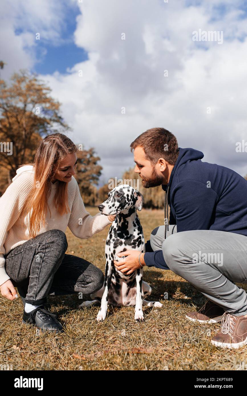 Coppia gioca con il suo cane dalmata a piedi nel parco Foto Stock