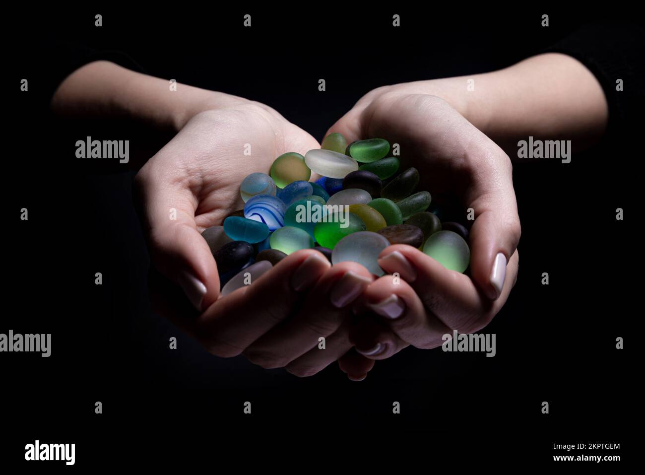 Mani con pietre colorate giovane donna sta tenendo una collezione di varie gemme minerali grezze nel suo palmo isolato su sfondo nero Foto Stock