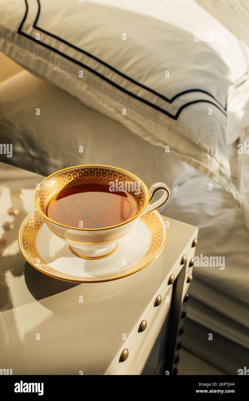 Tè nero in oro fantasia e bianco teacup nel pomeriggio sul comodino Foto Stock