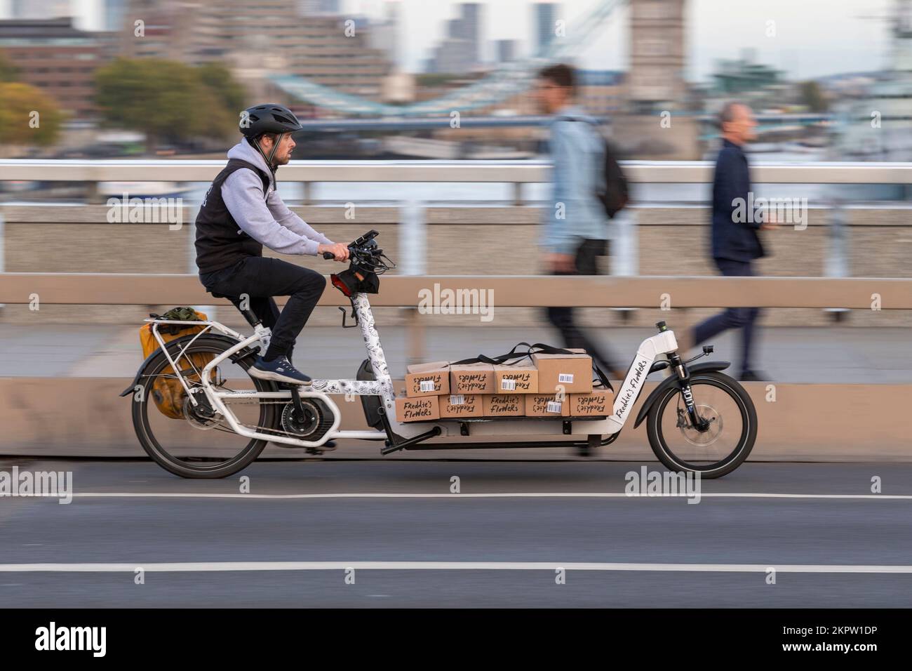 Un corriere ciclistico in sella a una bicicletta e-cargo carica di fiori, London Bridge, Londra, Regno Unito. 18 Ott 2022 Foto Stock