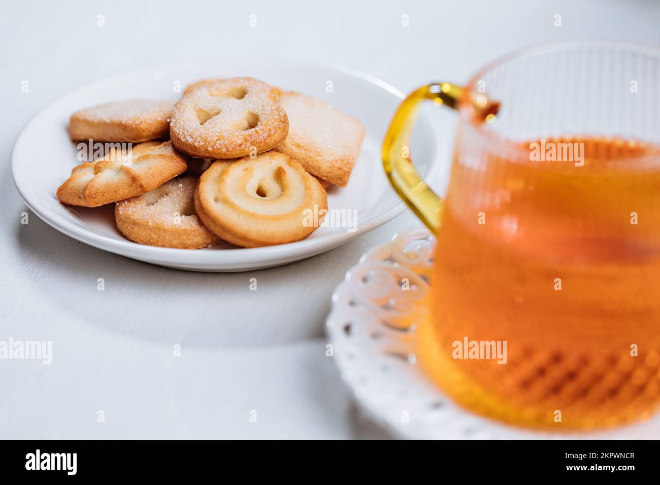 Biscotti e tè in tazza di vetro serviti nella luminosa atmosfera natalizia. Impostazione delle scene luminose e luminose. Foto Stock