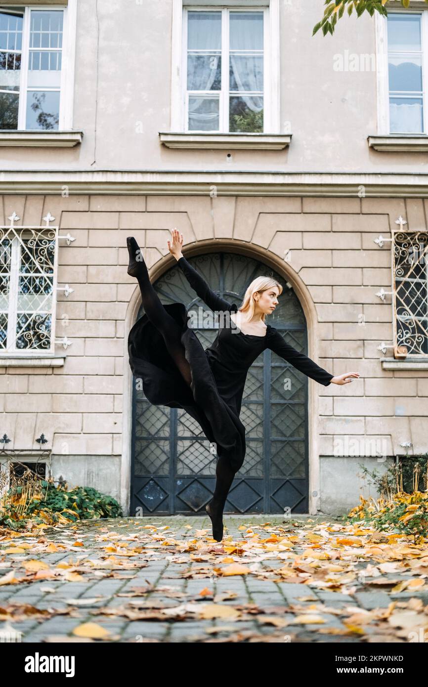 Ballerina Dancing in via autunnale città, ballerino moderno in vestito nero, Pointe Shoes Outdoors. Balsamo, balsamo quotidiano Foto Stock