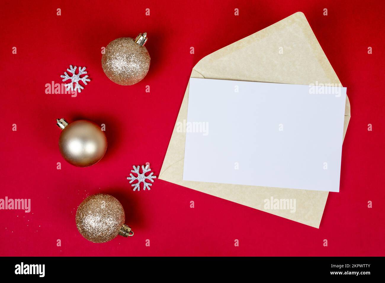 La lettera di Natale mock in su con la busta e la decorazione dorata delle sfere di natale su sfondo rosso con lo spazio della copia e i fiocchi di neve, vista dall'alto. Foto Stock