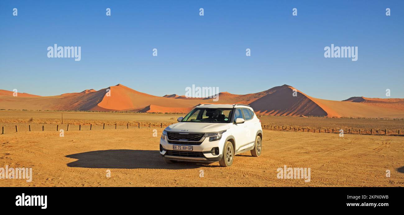 Namib Naukluft, Namibia, 2022. Un veicolo a noleggio bianco parcheggiato con ampie dune rosse sullo sfondo. I turisti possono auto intorno al parco e io Foto Stock