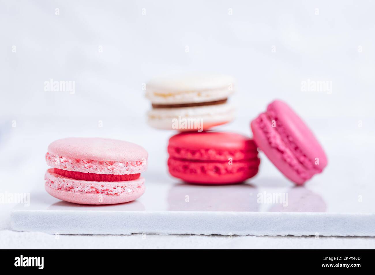 Primo piano di macaron in diversi colori su sfondo bianco luminoso con riflessi sottili sul vassoio in marmo Popolare dessert merengue con farcitura Foto Stock