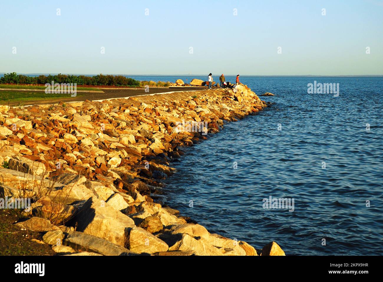 Una famiglia si trova ai margini di un molo di pietra che si affaccia sull'acqua lungo la costa del Connecticut Foto Stock