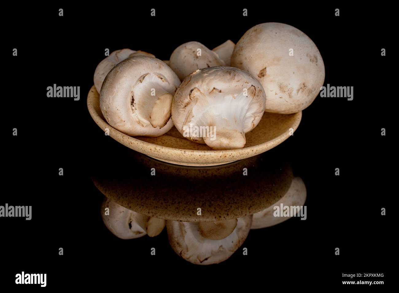 Diversi funghi champignon freschi e biologici su un piatto di ceramica, primo piano, su fondo nero. Foto Stock