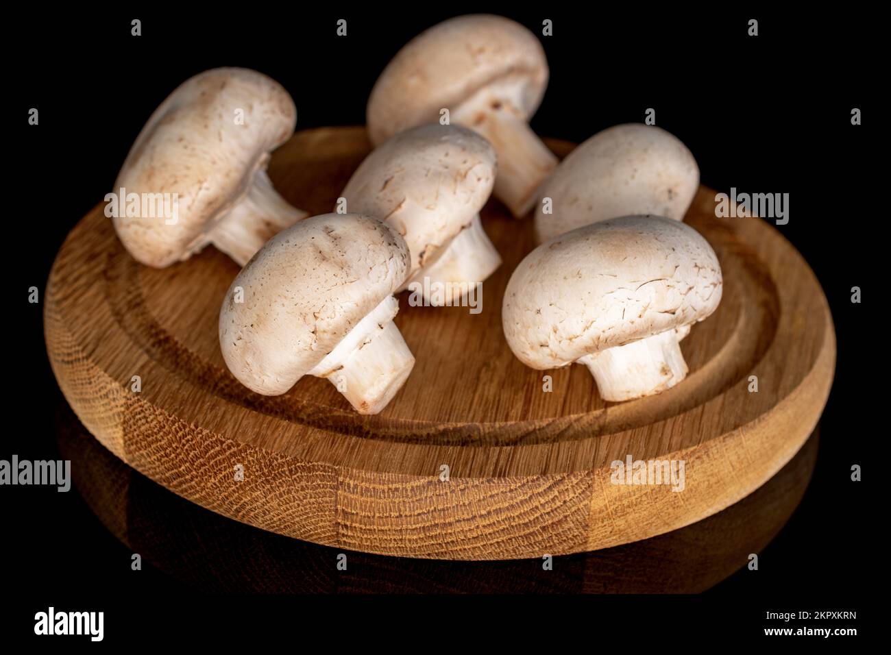 Diversi funghi champignon freschi e biologici interi su un vassoio rotondo di bambù, primo piano, su sfondo nero. Foto Stock