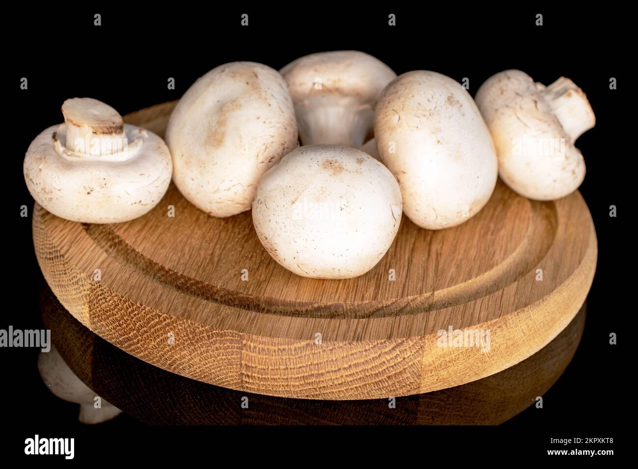 Diversi funghi champignon freschi e biologici interi su un vassoio rotondo di bambù, primo piano, su sfondo nero. Foto Stock