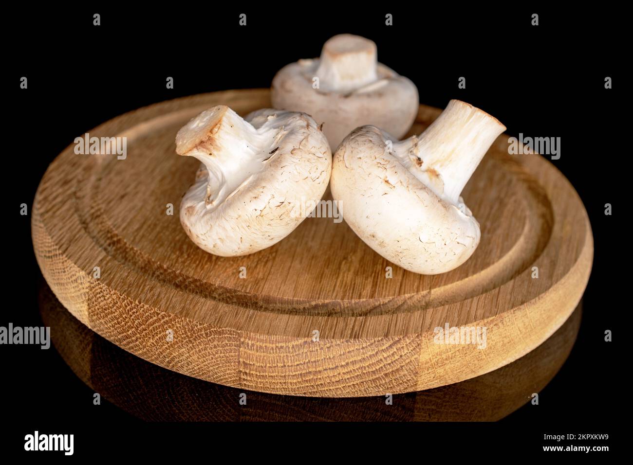 Tre funghi champignon freschi e biologici interi su un vassoio rotondo di bambù, primo piano, su fondo nero. Foto Stock