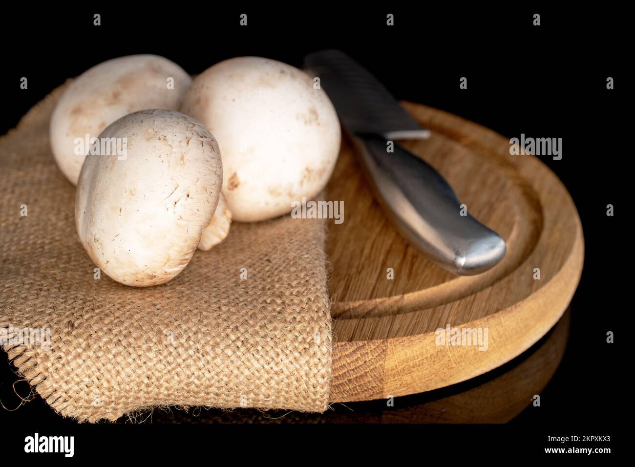 Tre funghi freschi e freschi, con un coltello di metallo su un vassoio rotondo di bambù, primo piano, su sfondo nero. Foto Stock